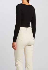 Schwarzes, geripptes Langarmoberteil, kombiniert mit hellbeigen, hochgeschnittenen Jeans mit Gesäßtaschen und körpernaher Silhouette.