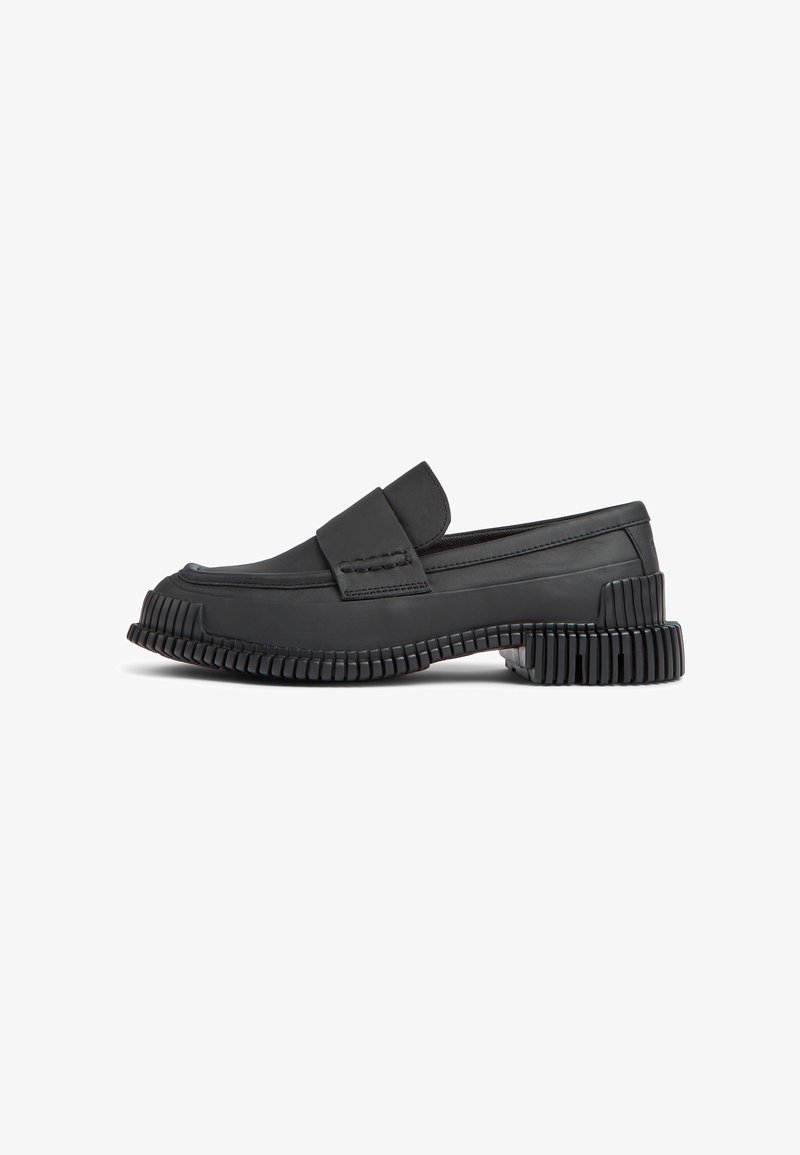 Mocassin noir à enfiler avec semelle épaisse rainurée et détail de bride sur le dessus, montré de profil sur un fond blanc.