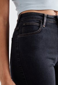 Vaqueros de color azul oscuro con un diseño ajustado, que cuentan con costuras naranjas, múltiples bolsillos y una cintura alta. Textura de mezclilla suave.