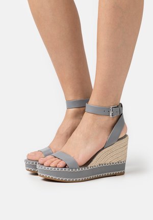 Grå kile-sandaler med en flettet jute-hæl og ankelrem. Overdelen har en glat læderlignende tekstur og hvid syning.