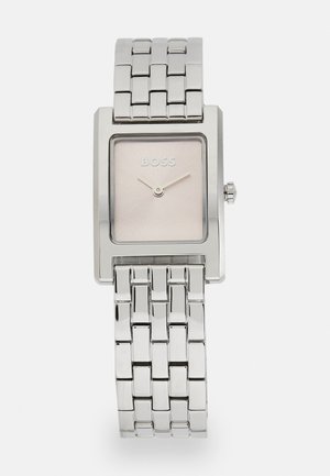 Montre rectangulaire argentée avec un cadran rose clair lisse, arborant le nom de la marque "BOSS", et un bracelet en métal maillé avec une finition polie.