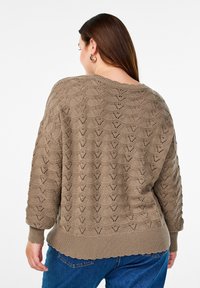 Knitted sweater in light brown with a textured, patterned design. Features a wide neckline and ribbed cuffs and hem. Loose-fitting silhouette.