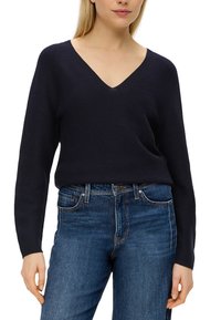 Navy V-Ausschnitt-Pullover aus strukturiertem Strickstoff, mit langen Ärmeln und lässiger Passform, kombiniert mit klassischen blauen Jeans.