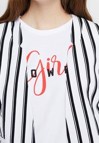 Pasiasty czarno-biały otwarty kardigan zestawiony z białą koszulką z wyraźnym czerwonym i czarnym napisem "Girl Power."