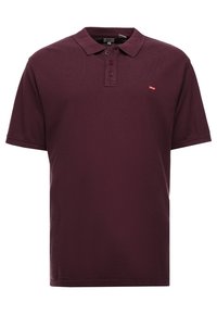 Polo en bourgogne en coton, avec un col classique, une patte de boutonnage à trois boutons, et un petit logo rouge sur la poitrine gauche. Manches courtes.