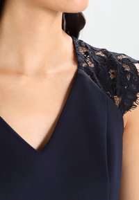 Navy dress with a deep V-neckline, featuring delicate black lace sleeves and smooth fabric, highlighting the shoulder area.