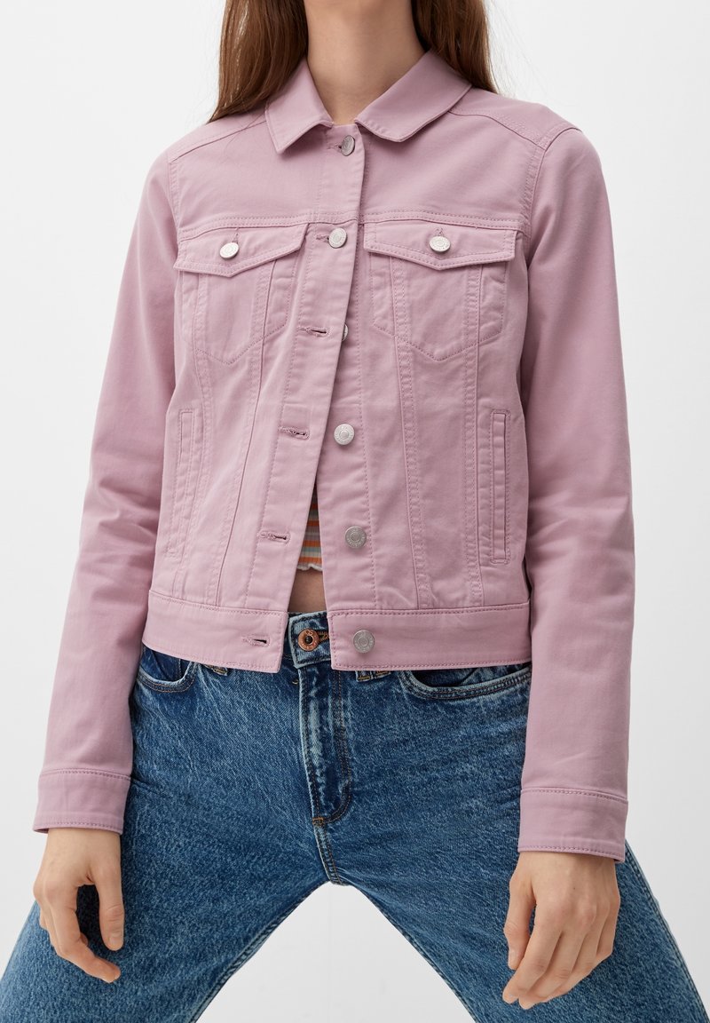 Chaqueta de mezclilla rosa con cuello, dos bolsillos frontales y botones plateados. Tejido texturizado, diseño ajustado y longitud corta combinada con jeans azules.