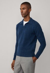 Navyblauwe gebreide trui met een kraag en geribbelde manchetten en zoom. Beschikt over een textuurpatroon met kleine, multikleurige stippen.