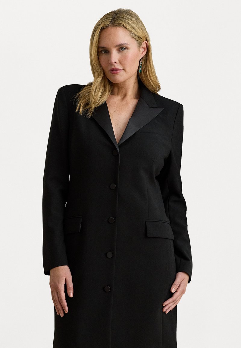 Melnā pielāgotā mēteli ar garām piedurknēm, ar iespiestu atlokiem, piecu pogu aizdari, divām priekšējām kabatām un nedaudz teksturētu audumu.