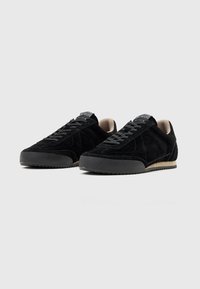 Schwarze Wildleder-Sneaker mit niedrigem Profil, Schnürdesign, strukturierter schwarzer Sohle und gepolstertem Innenfutter.