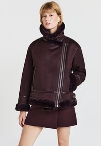 Bordeauxrote Lammfelljacke mit hohem Kragen, Reißverschluss und Pelzbesatz an Bündchen und Saum, mit strukturierter Silhouette und glatter Textur.