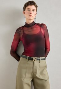 Top trasparente a maniche lunghe con un ombre gradient che va dal rosso scuro al nero, caratterizzato da spalle arricciate, abbinato a pantaloni beige a vita alta e una cintura.
