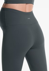 Sötétszürke leggings sima, rugalmas anyagból, magas derékkal és minimális logózással a derékrészen.