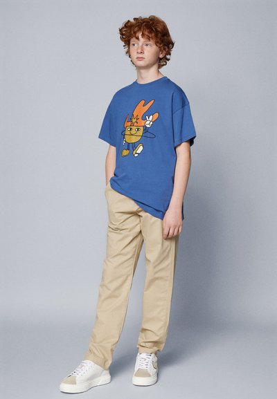 Sinine puuvillane T-särk, millel on multikakujutis, koos beezide pükstega ja valgete tossudega. Pehme tekstuur, mugav iste.