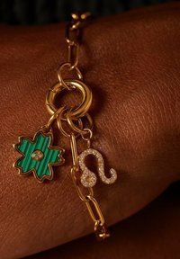 Gouden kettingarmband met een groen gestreepte bloemenbedel met een edelsteen en een sprankelende dierenriem charm. Smooth textuur, gedetailleerde accenten.