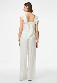 Top di crema chiara con maniche a volant, schiena scoperta e vestibilità ampia, abbinato a pantaloni larghi e fluidi dello stesso colore. Texture morbida.