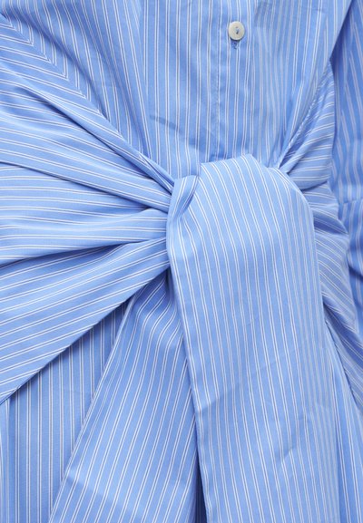 Μπλε υφασμάτινο ραβδωτό δεμένο σε μεγάλο κόμπο με εμφανές λευκό κουμπί σε ένδυμα.