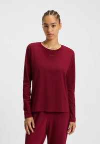 Långärmad skjorta i djupt burgundy, tillverkad av ett mjukt tyg. Den har en rund hals och en diskret logotyp tryckt på framsidan.