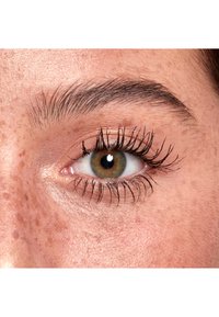 Primo piano di un occhio marrone con ciglia lunghe, circondato da pelle marrone chiaro e peli fini delle sopracciglia, che mostra lentiggini e una texture liscia.