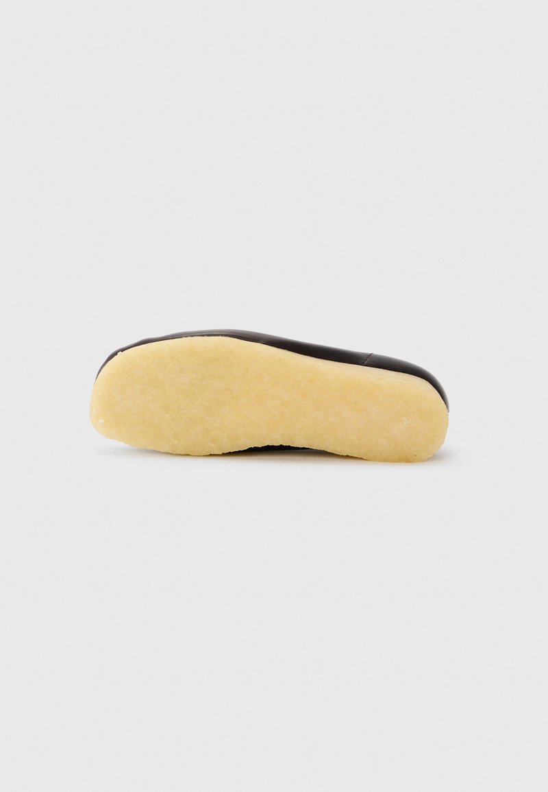 Chaussure noire avec un dessus lisse et une semelle beige contrastante. La semelle présente une surface texturée et une forme arrondie.