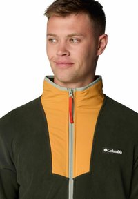 Fleece jacket featuring a green body and a yellow high collar, silver zipper, and an orange zipper pull; Columbia logo on the chest.