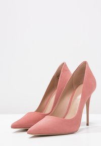 Talons hauts en daim rose avec un bout pointu, un talon stiletto fin et un design épuré. Texture lisse avec des accents minimalistes et un intérieur nude.