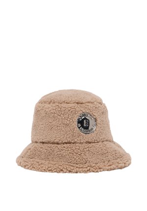 Beige fuzzy bucket hat with a round silver badge on the front featuring an engraved design and text.