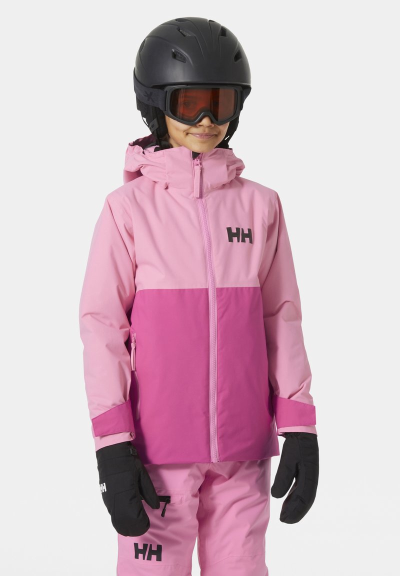 Růžová lyžařská bunda s dvoubarevným designem, která má tmavší dolní polovinu a černé logo. Vybavena černými rukavicemi a helmou.