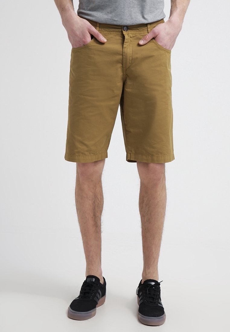 Shorts khaki en coton, avec un devant plat, deux poches latérales et une coupe régulière, portés avec des baskets noires.