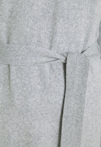 Wrap grigio chiaro lavorato a maglia con superficie testurizzata, dotato di una cintura annodata e materiale morbido e flessibile per il comfort.