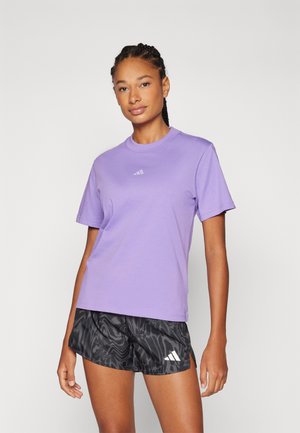 Camiseta de algodón morada de manga corta, con cuello redondo y un pequeño logo en el pecho. Combinada con pantalones cortos negros con un patrón que presentan aberturas laterales.