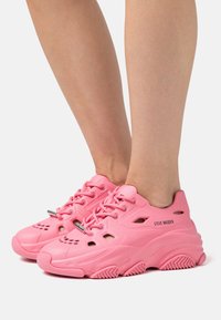 Sneaker rosa con finitura testurizzata, design con lacci e fori di ventilazione. Presenta una suola spessa e pronunciata con grip. Marchio "STEVE MADDEN".