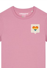 Hellrosa Baumwoll-T-Shirt mit einem kleinen Herzdesign in Regenbogenfarben, das sich in einer Sprechblasenform auf der linken Brustseite befindet.