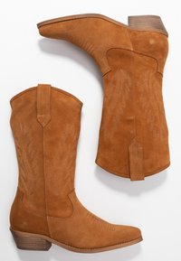 Jasnobrązowe zamszowe kowbojki z szpiczastym noskiem, warstwowym drewnianym obcasem oraz dekoracyjnym haftem przedstawiającym wzory liści na cholewce.