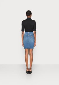 Minifalda de mezclilla con cintura alta, lavado azul, cremallera trasera y dos bolsillos en la parte posterior. Combinada con una blusa negra ajustada y sandalias de tacón.