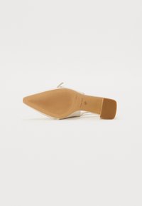 Beige høyhælte sko med spiss tå og smal stropp. Teksturert såle med merkevaredetalj. Glatt overmateriale. Chunky hælbase.