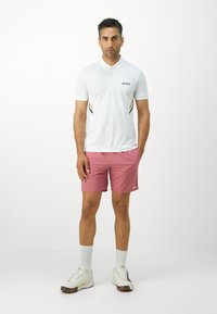 White short-sleeve polo with black "BOSS" logo and gold accents, paired with pink shorts and white sneakers with multicolor details.