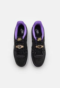 Svarta sneakers med lila detaljer, ovandel i läder, vita sula och guldaccessoarer. Har perforerade detaljer och en texturerad yta.