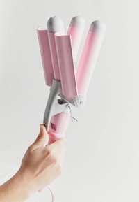 Drie-vat krulijzer met roze keramische vaten, witte accenten en een textuurgrip in het grijs; beschikt over een aan/uit-knop en een draad.