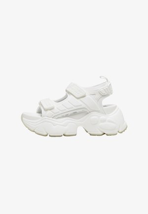 Bílá sportovní sandále s nastavitelnými suchými zipy, polstrovanou podrážkou, otevřeným designem, tlustým profilem a texturovanými detaily. Lehký syntetický materiál.