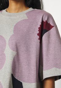 Jasnoszara, oversize koszulka z dużymi kwiatowymi wzorami w odcieniach różowego, burgundowego i czarnego. Miękka tkanina z okrągłym dekoltem.
