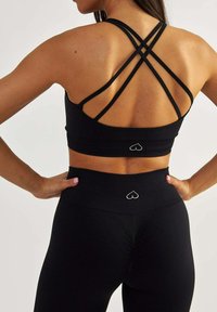 Czarny sportowy top z krótkim rękawem, z krzyżującymi się ramiączkami i detalem z logo serca. Połączony z czarnymi legginsami z wysokim stanem, z podobnym logo.