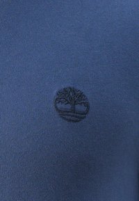 Țesătură tricotată de culoare bleumarin, cu un logo subtil negru al unui copac și o bază circulară, centrat pe îmbrăcăminte, cu o textură netedă.