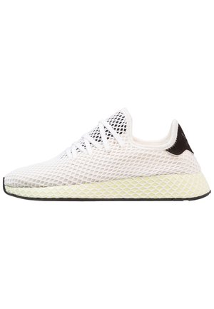 White low-top sneaker with mesh overlay, lace-up front, black heel detail, and textured light yellow sole on a white background.