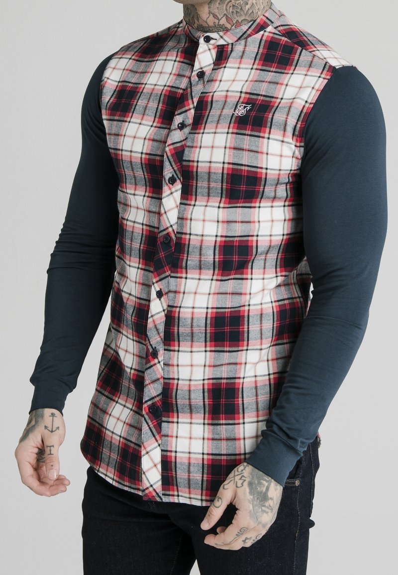 Koszula w kratę w czerwone, czarne i białe wzory. Długie granatowe rękawy, zapinana na guziki z haftowanym logo na piersi.