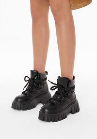 Baskets montantes en cuir noir avec des semelles épaisses et crantées, un système de laçage à l'avant et un col rembourré. Texture lisse avec des accents minimes.