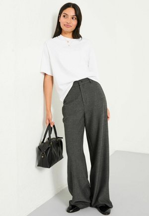 Weißes Kurzarmhemd kombiniert mit lockeren, grauen Nadelstreifenhosen und einer schwarzen Handtasche. Der Look wird mit glänzenden schwarzen Schuhen abgerundet.