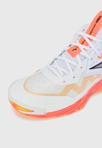 Hvid sportsko med mesh-overdel, orange detaljer og en struktureret sål i nuancer af pink og gul. Bemærkelsesværdigt zigzag-design.