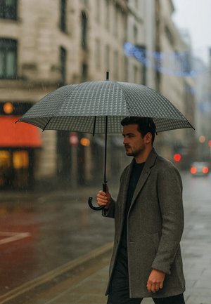 Black umbrella with a textured, checkered pattern, held by a person in a gray coat, walking on a wet street in rainy weather.