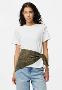 Hvid T-shirt, lys blå denim jeans og et olivengrønt bælte i tekstureret stof bundet omkring livet. Bæltet har et vævet mønster.